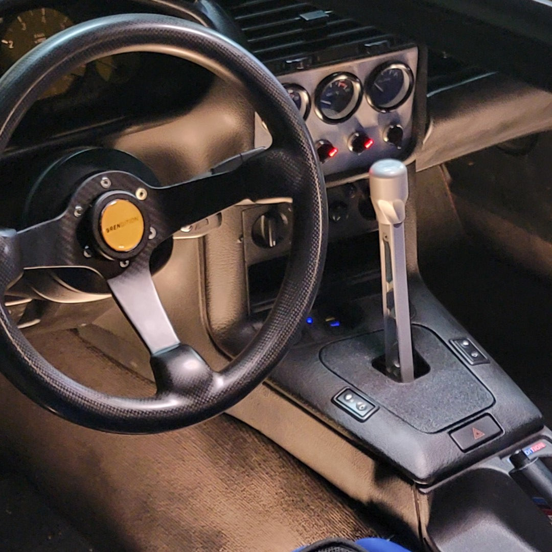 A black BMW E36 shift boot cover with a textured finish, installed in a vehicle's interior.